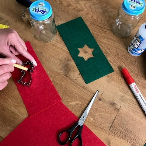 Roter und grüner Filz auf Holztisch, auf dem roten Filz wird von einer Hand ein Tannenbaum vorgezeichnet