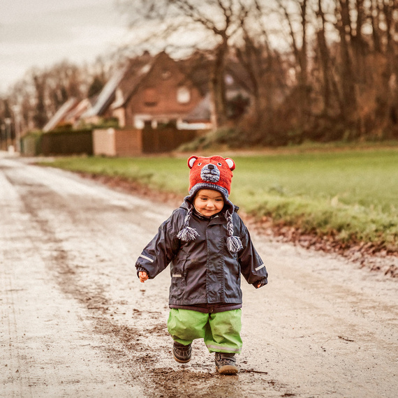 Alete Baby in Regenhose spielt im Matsch