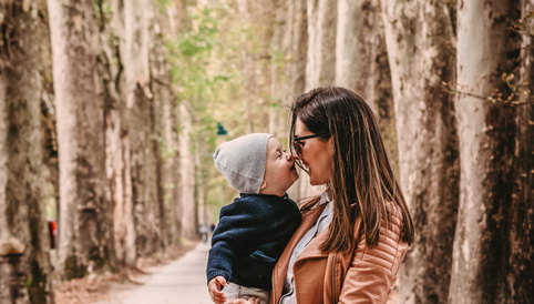 Mutter und Sohn in einer Baumallee, sie lächeln sich an und berühren sich mit den Nasen. Herbstliche Atmosphäre.