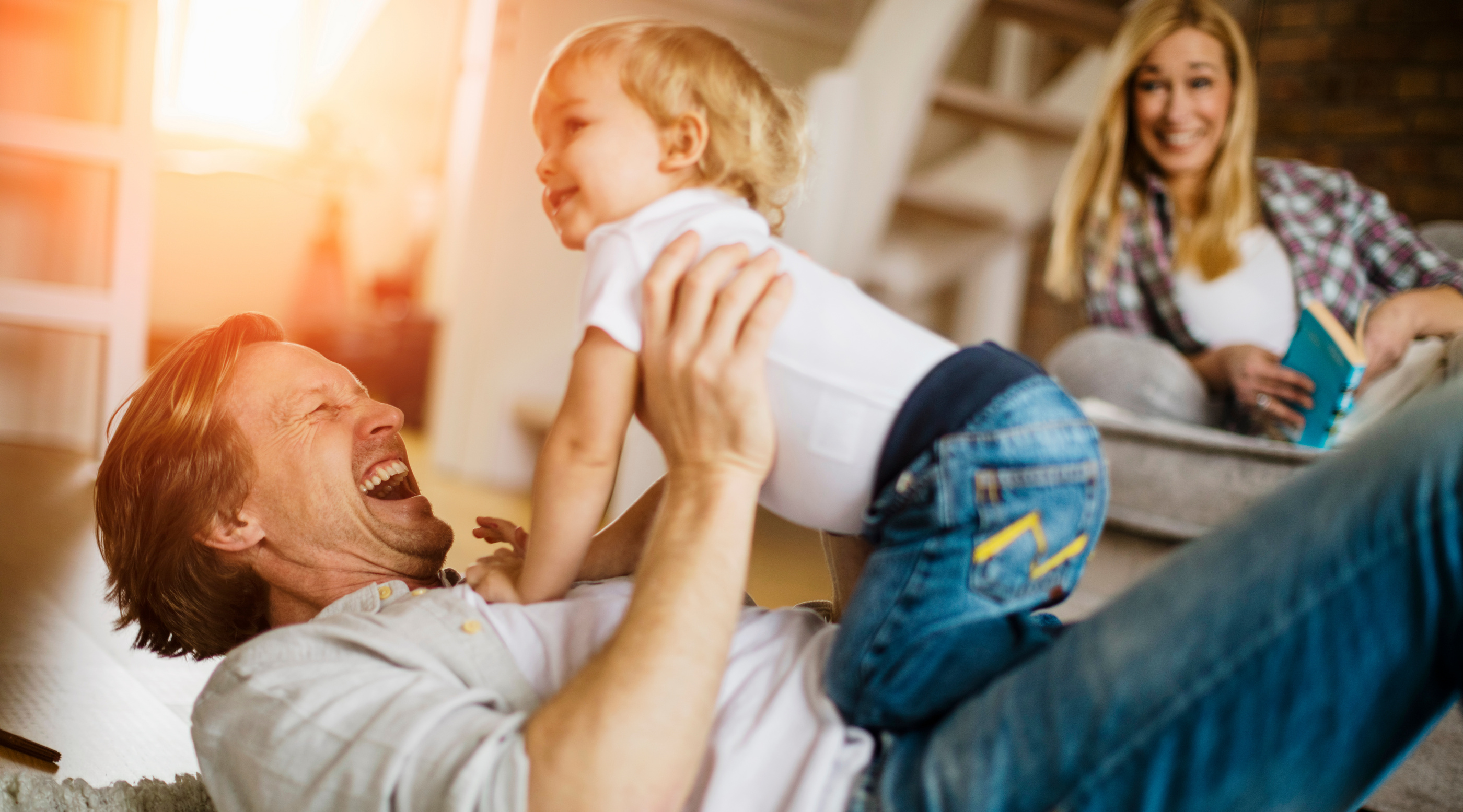 Lachender Vater spielt mit seinem kleinen Sohn auf dem Boden eines hellen, modernen Wohnzimmers.