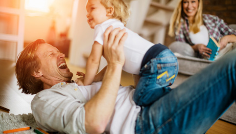 Lachender Vater spielt mit seinem kleinen Sohn auf dem Boden eines hellen, modernen Wohnzimmers.
