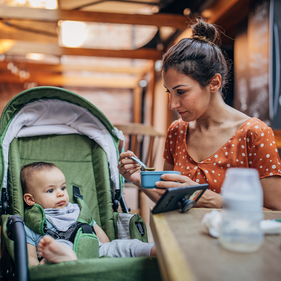 Mama füttert Baby im Kinderwagen an einem Tisch in einem Cafe sitzend