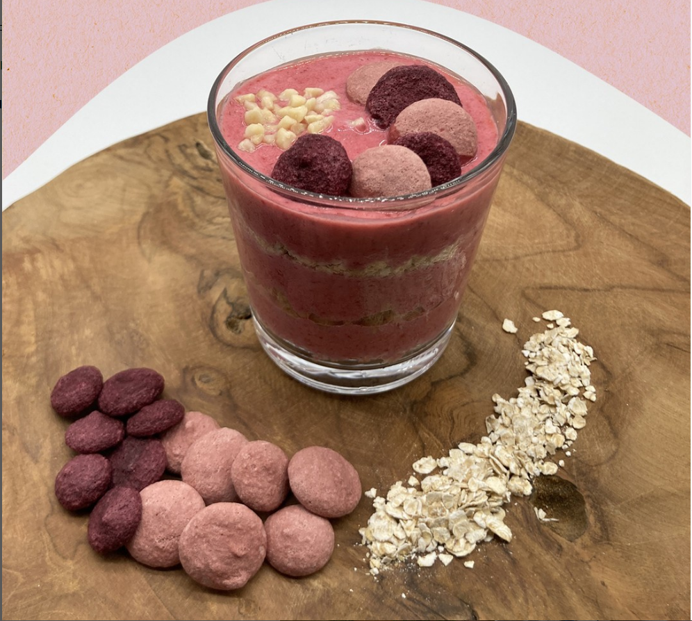 Schüssel mit Erdbeersmoothie, dekoriert mit knusprigen Keksen und Haferflocken auf Holzunterlage.