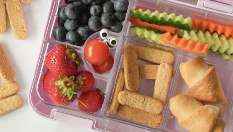 Bunt gefüllte Lunchbox mit frischen Blaubeeren, Erdbeeren, Paprika, Gurken und herzhaften Snacks. Ideal für gesunde Mahlzeiten.