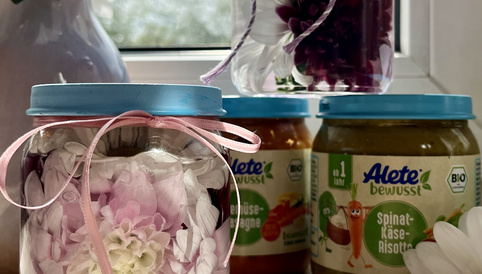 Gläser mit bunten Blumenarrangements und Babygläschen von Alete auf einer Fensterbank, umgeben von weißen Blumen.