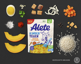 Alete Kinder Teller Risotto mit Kürbis, umgeben von frischen Zutaten wie Kürbisstücken, Reis, Zwiebeln, Karotten und Gewürzen auf einem dunklen Hintergrund.