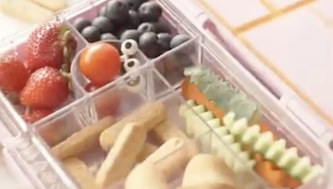 Bunt gefüllte Lunchbox mit frischen Erdbeeren, Blaubeeren, Kirschtomaten, Gemüsesticks und Käsehörnchen. Ideal für gesunde Snacks.