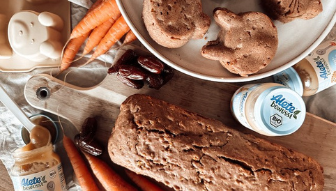 Karottenkuchen in Kasten- und Hasenform liegt auf Holzbrett, daneben Karotten und Alete-Gläschen