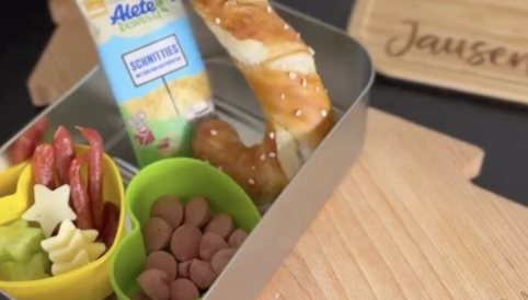 Ein Snack-Bento mit Brezel, Wurststückchen, Gemüse-Sticks, einem Trockenfrüchte-Snack und einer Tüte Snacks.
