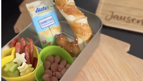 Jausenbox mit Brezel, Snackkeksen und buntem Gemüse, ideal für unterwegs oder als Pausenmahlzeit.
