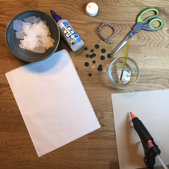 Bastelmaterialien auf einem Tisch: Schere, Klebstoff, Papierschnipsel, Aufkleber, Pinsel, Glas mit Wasser und Draht.