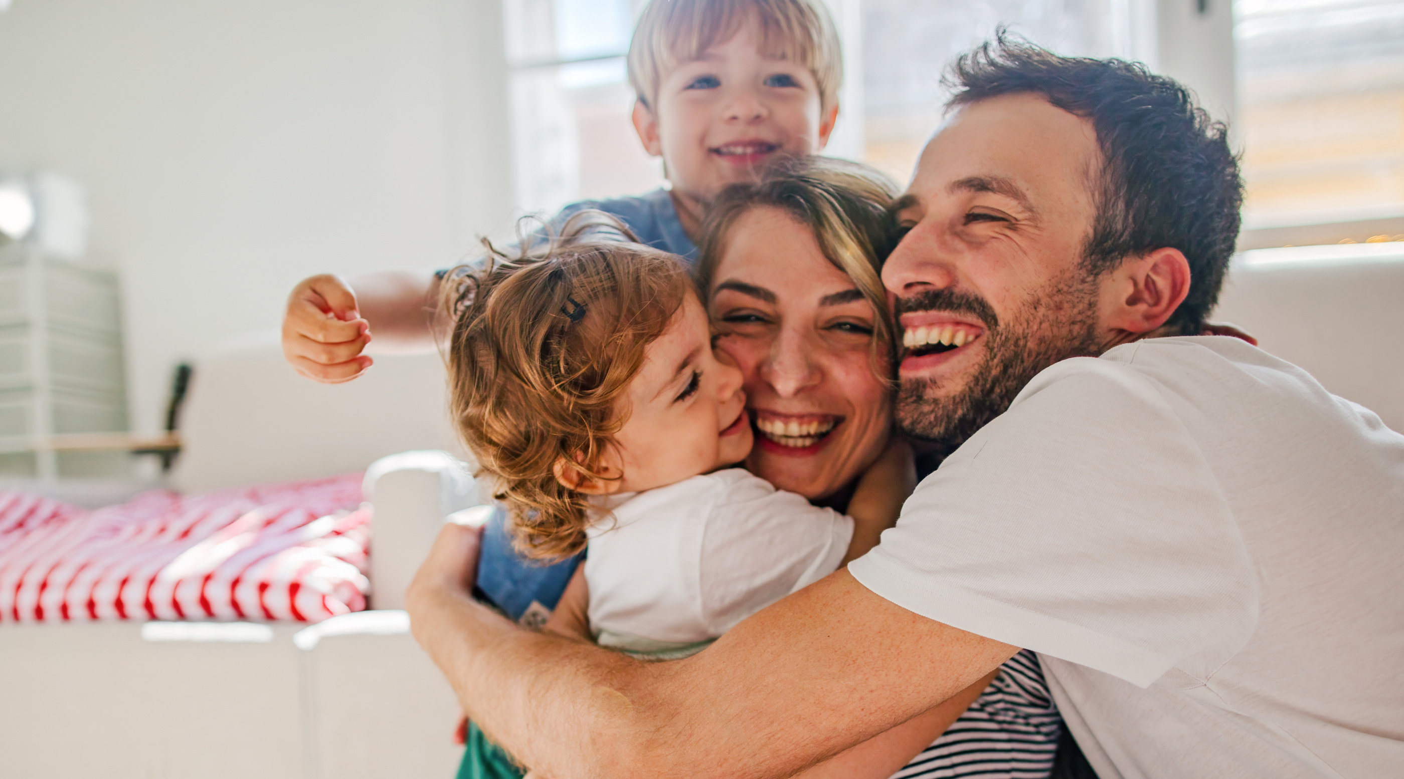 Familie umarmt sich lachend in einem heller eingerichteten Raum. Kinder zeigen Freude und Zuneigung.