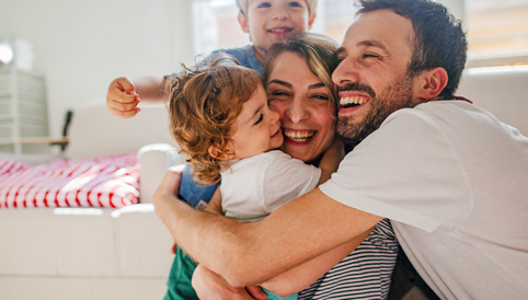 Familie umarmt sich lachend in einem heller eingerichteten Raum. Kinder zeigen Freude und Zuneigung.