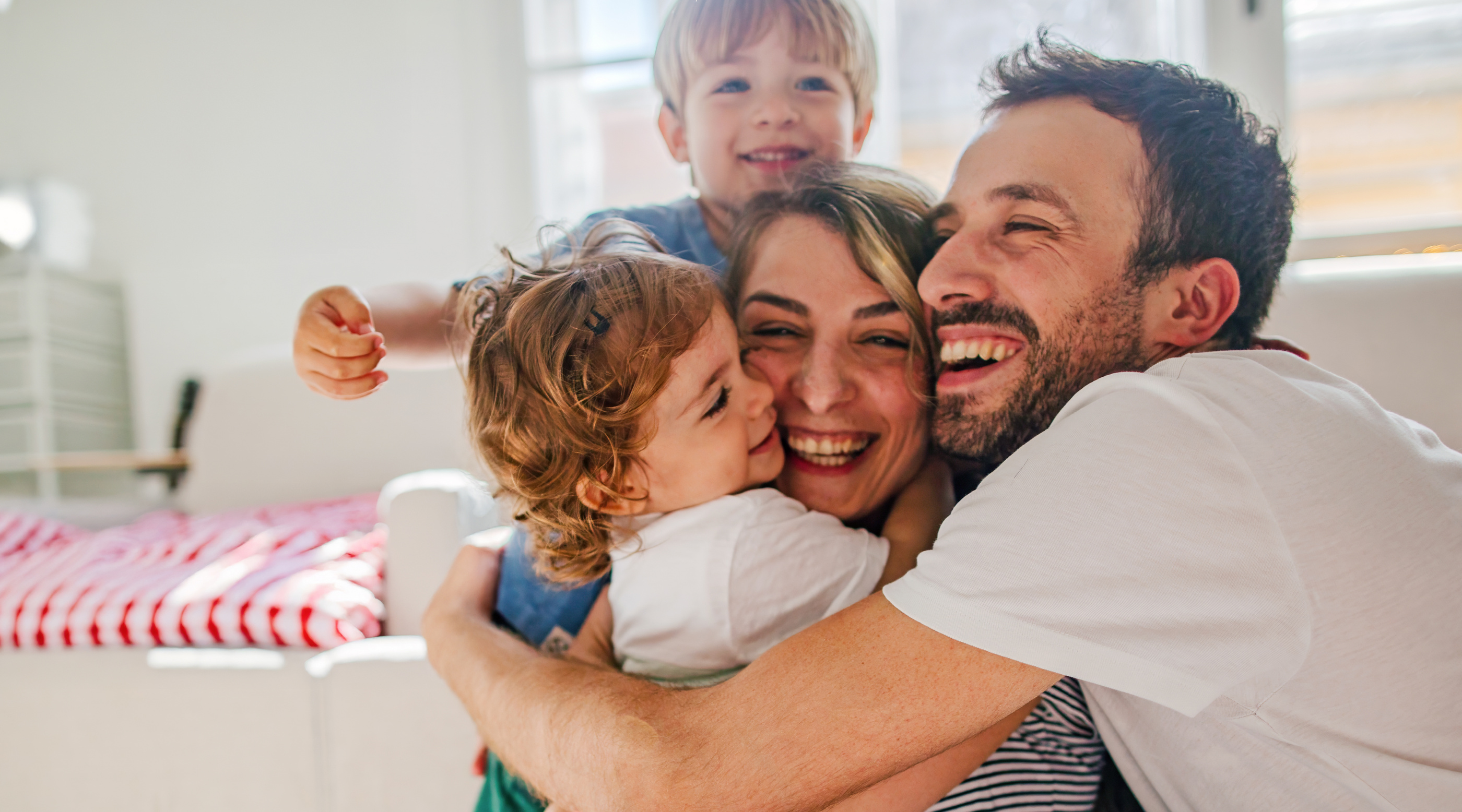 Familie umarmt sich lachend in einem heller eingerichteten Raum. Kinder zeigen Freude und Zuneigung.
