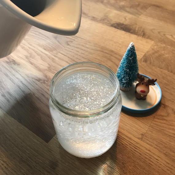 Glas mit sprudelndem Wasser auf einem Holztisch, daneben eine kleine Weihnachtsdeko mit einem blauen Baum und einem Rentier.