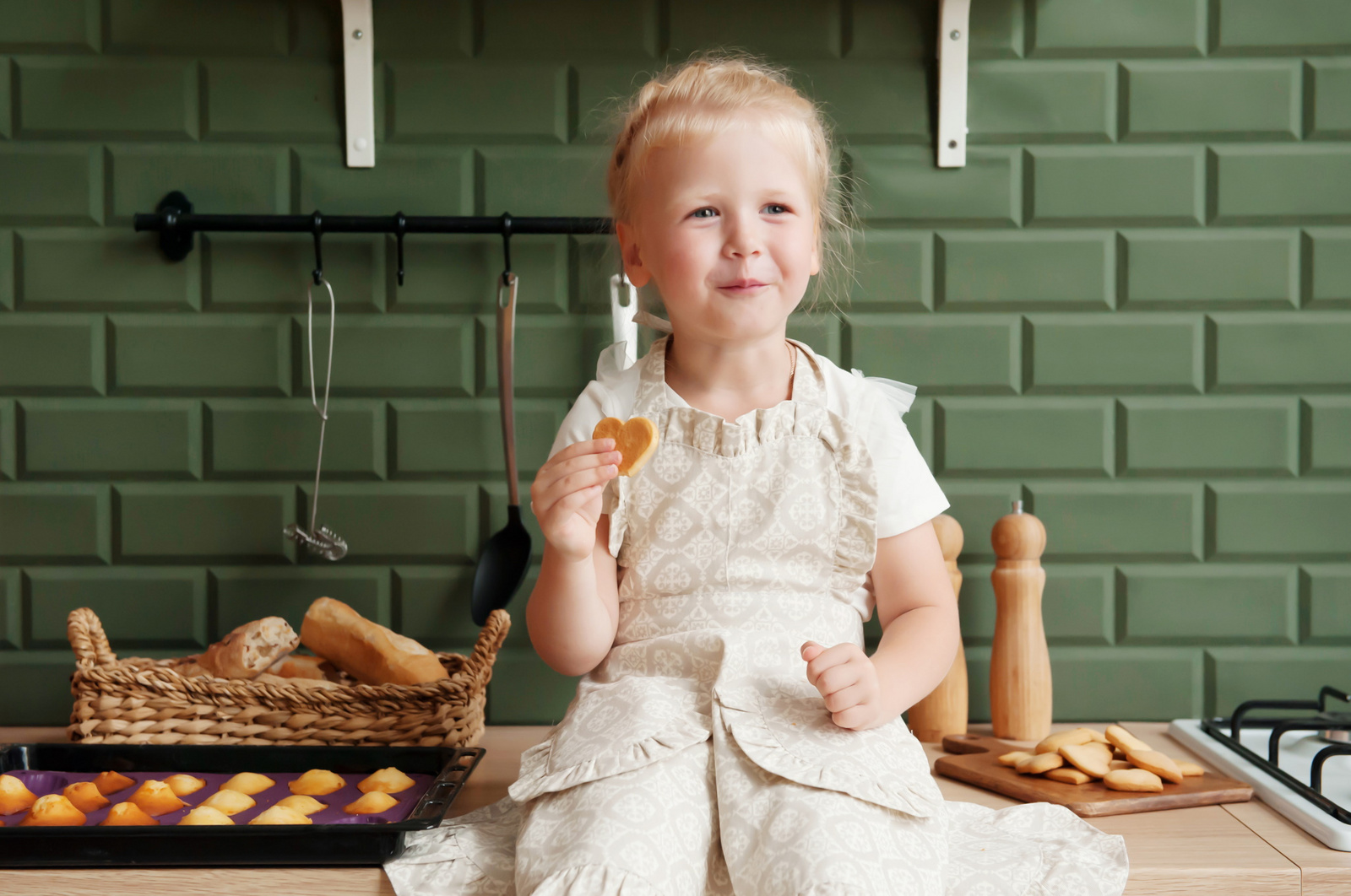ädchen sitzt auf der Küchenzeile und isst selbstgebackene Kekse