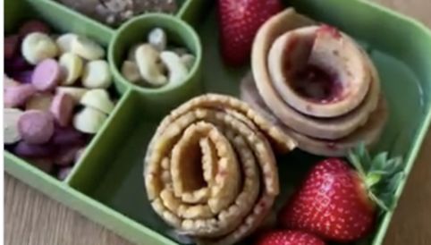 Gesunde Snack-Box mit frischen Erdbeeren, Pfannkuchenrosen und verschiedenen Süßigkeiten in einer grünen Brotdose
