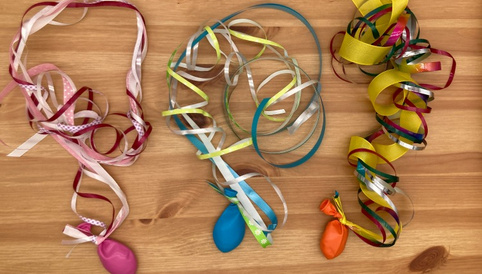 Bunte Bänder mit kleinen Ballons am Ende festgeknotet auf Holztisch