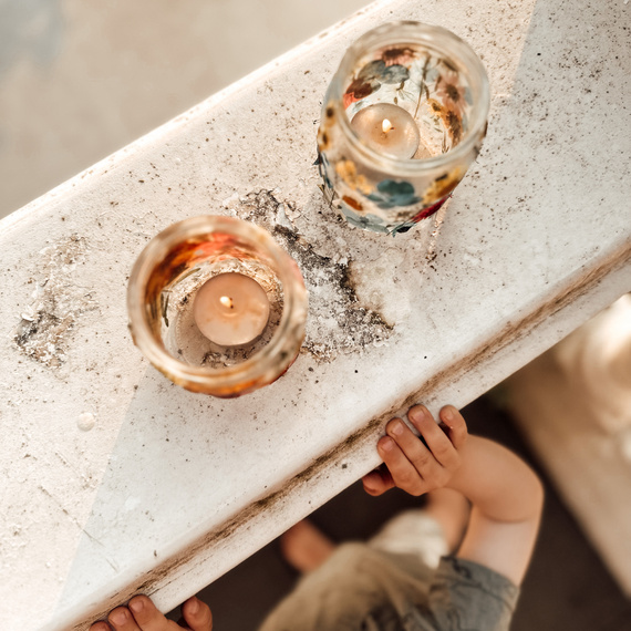 Ein Kind schaut von oben auf zwei Kerzen in dekorativen Gläsern, die auf einer abgenutzten Oberfläche stehen.