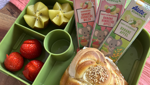 Gesunde Lunchbox mit frischen Erdbeeren, geschnittenen Äpfeln und drei Alete Snackriegeln in einer grünen Box.