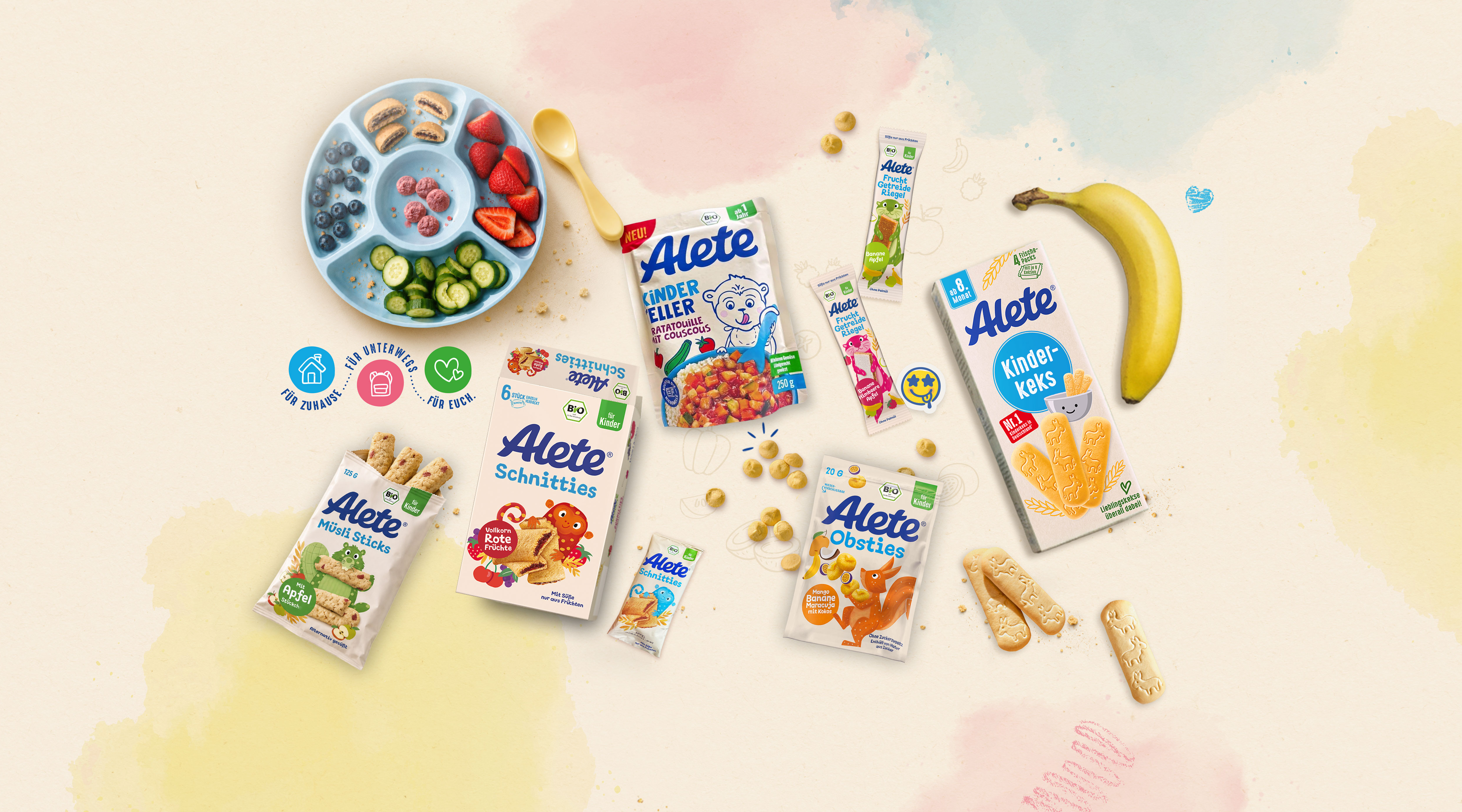 Eine Auswahl an Alete-Kinderprodukten, darunter Snacks, Kuchen und ein Teller mit gesunden Früchten und Gemüse, auf einem sanften Hintergrund.