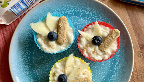 Muffins in bunten Förmchen mit Birnenscheiben, Heidelbeeren und Alete Müslisticks auf blauem Teller.