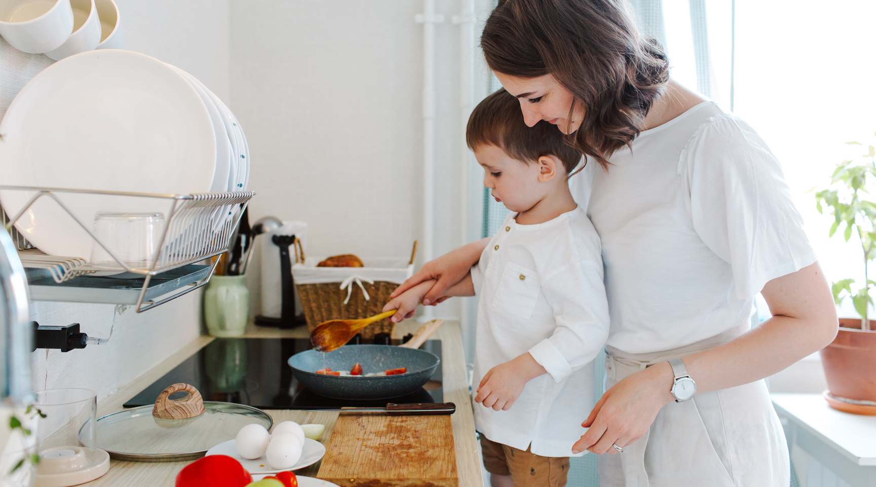Junge hilft seiner Mutter beim Kochen in einer modernen Küche, während sie gemeinsam Zutaten in einer Pfanne zubereiten.