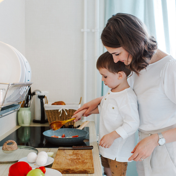 Junge hilft seiner Mutter beim Kochen in einer modernen Küche, während sie gemeinsam Zutaten in einer Pfanne zubereiten.
