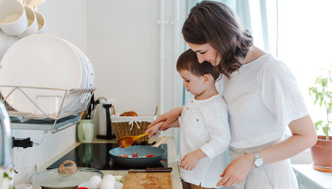 Junge hilft seiner Mutter beim Kochen in einer modernen Küche, während sie gemeinsam Zutaten in einer Pfanne zubereiten.