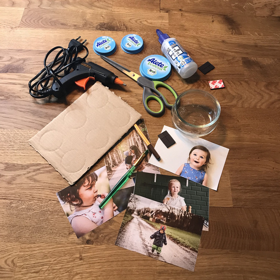 Materialien für ein Bastelprojekt, darunter Fotos von Kindern, Schere, Kleber, Stift und eine Klebepistole auf einem Holztisch.