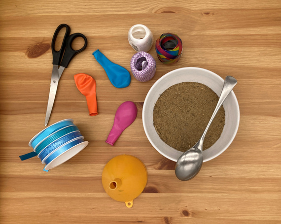 Bastelmaterialien aus bunten Ballons, Scheren, Bändern und einer Schüssel mit Sand auf Holztisch