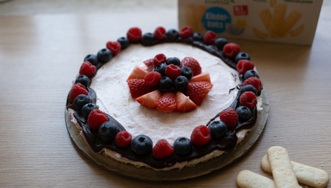 Käsekuchen mit Himbeeren und Blaubeeren, dekoriert mit Schokoladenglasur, auf Holzoberfläche platziert.