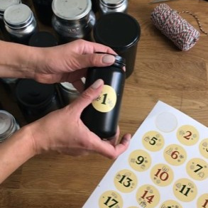 Hand klebt Zahlenpunkt auf Glas, im Vordergrund liegt Zettel mit Klebepunkte 