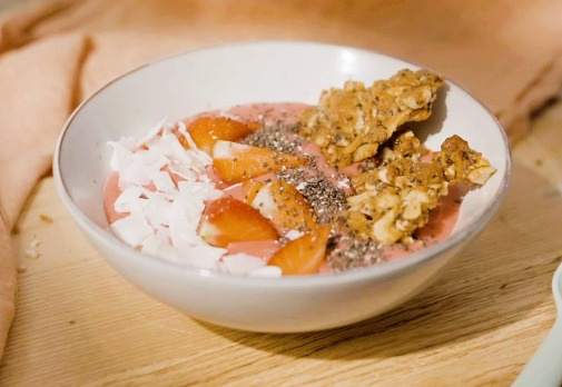 Fruchtige Smoothie-Schüssel mit Erdbeeren, Kokosraspeln, Chiasamen und knusprigen Müsliriegelstücken.