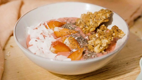 Fruchtige Smoothie-Schüssel mit Erdbeeren, Kokosraspeln, Chiasamen und knusprigen Müsliriegelstücken.
