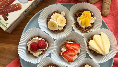 Bunte Kekstörtchen mit einer Schicht Quark und verschiedenen Früchten, serviert auf einem Teller mit Alete Kinder-Keksen und einem Glas Milch.