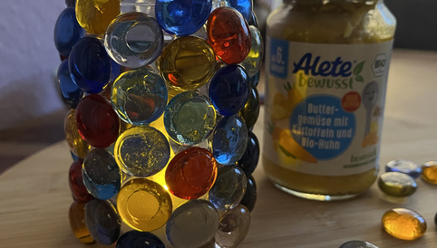 Bunt verziertes Aletegläschen mit leuchtenden Steinen neben einem Glas ALETE Buttergemüse.