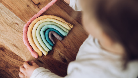 Bunte Knetebogen in Regenbogenform auf einem Holztisch, während ein Kind damit spielt.