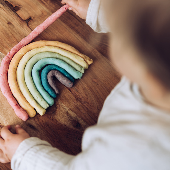 Bunte Knetebogen in Regenbogenform auf einem Holztisch, während ein Kind damit spielt.