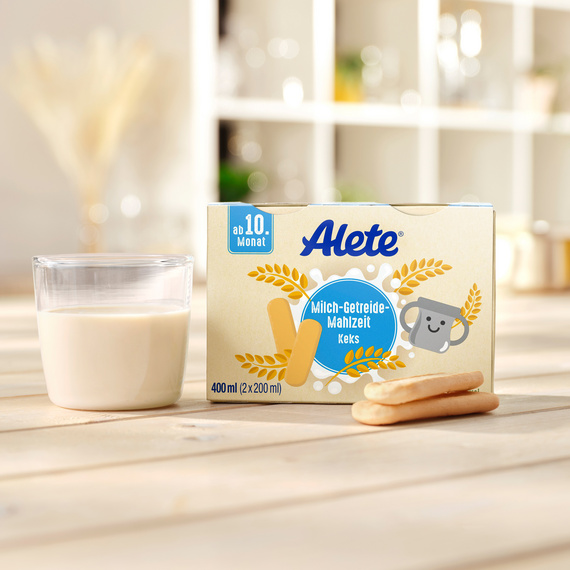 Milch-Getreide-Mahlzeit Kekse von Alete mit Glas Milch auf einem Tisch, geeignet für Babys ab 10 Monaten.