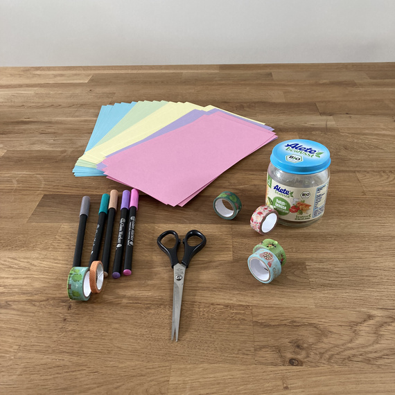 Bunte Papierblätter in verschiedenen Farben, Marker, Scheren und Klebebänder auf einem Holztisch, geeignet für Bastelprojekte.