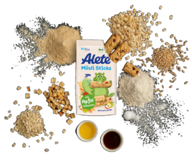 Alete Müsli Sticks umgeben mit einer Vielzahl von Zutaten wie Hafer, Apfelstückchen und verschiedenen Mehlen auf schwarzem Hintergrund.