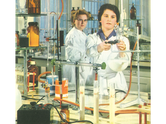 Zwei Wissenschaftlerinnen in Laborkitteln führen Experimente in einem chemischen Labor durch, umgeben von Glaswaren und chemischen Reagenzien.