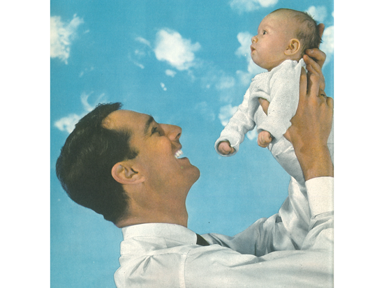 Vater hält lächelnd ein Baby vor einem blau-weißen Himmel mit Wolken.