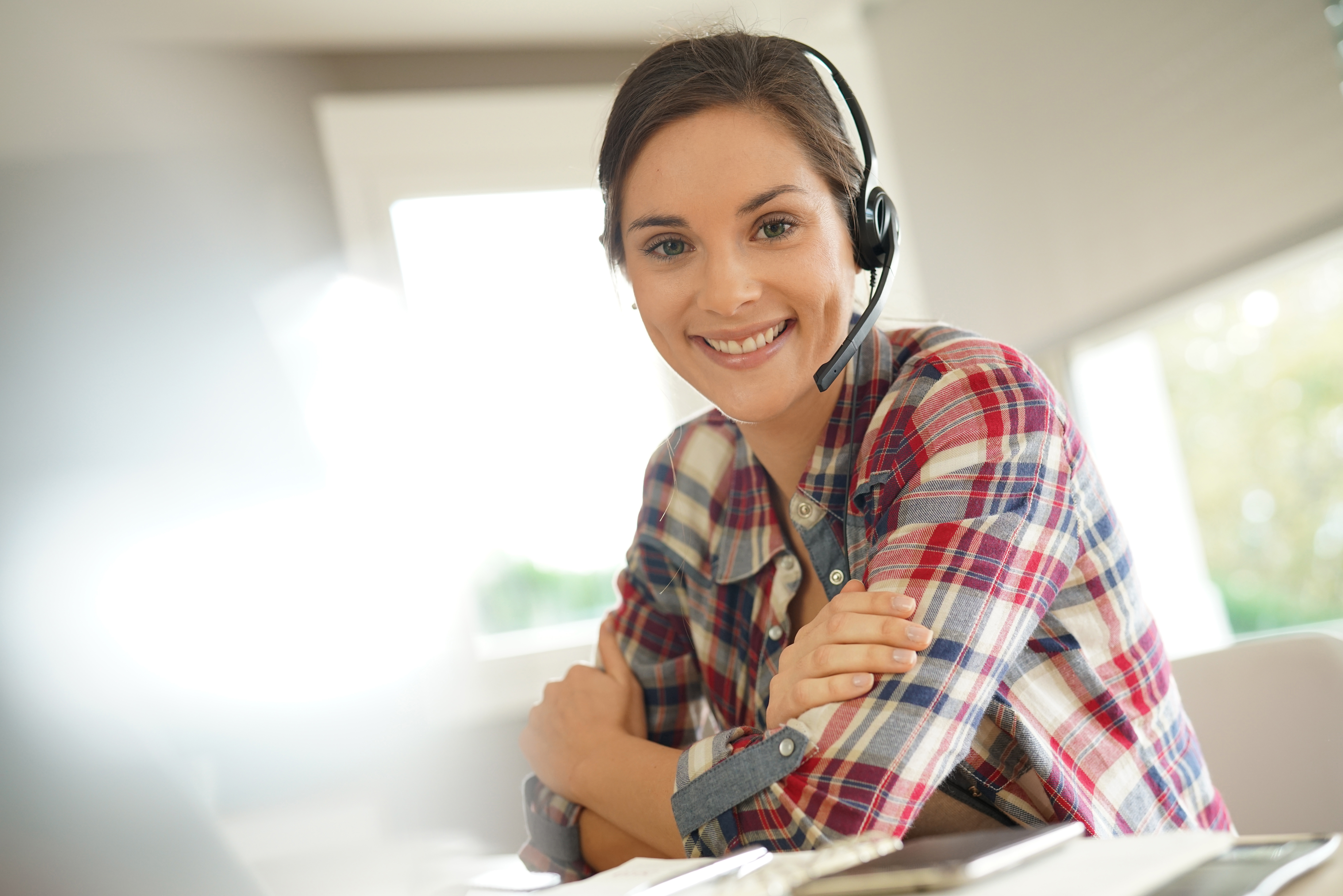 Lächelnde Frau mit Headset, die in einem modernen Büro am Schreibtisch sitzt und bereit für einen Kundenanruf ist.