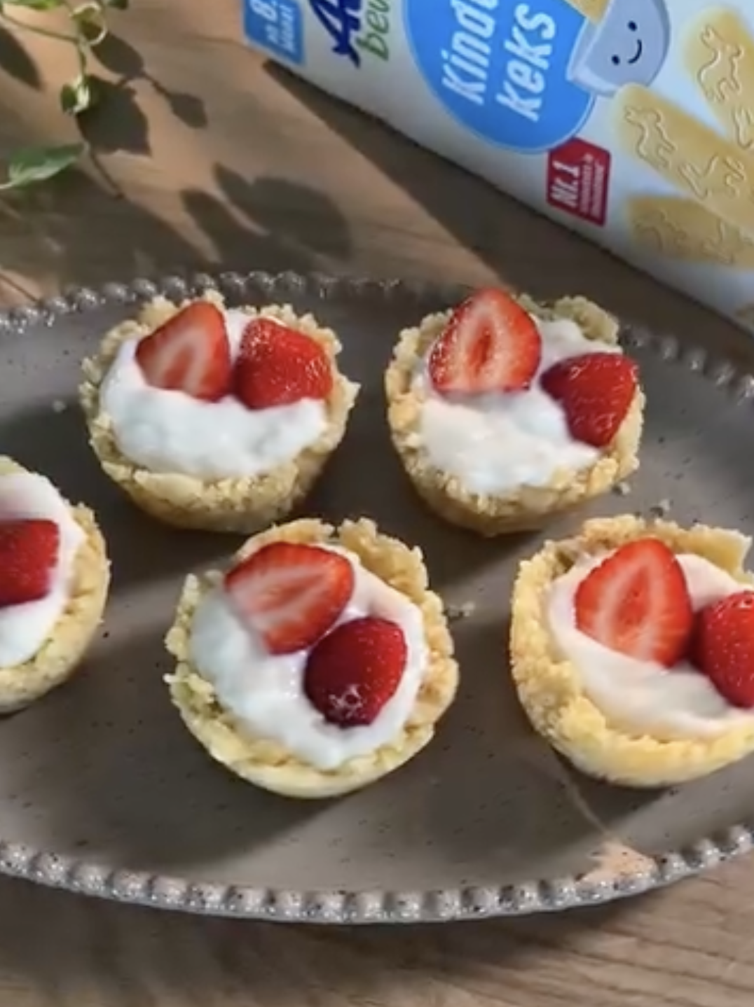 Mini-Keks-Delights mit Grießbrei und frischen Erdbeeren auf einem Teller, dekoriert mit grünen Pflanzen im Hintergrund.
